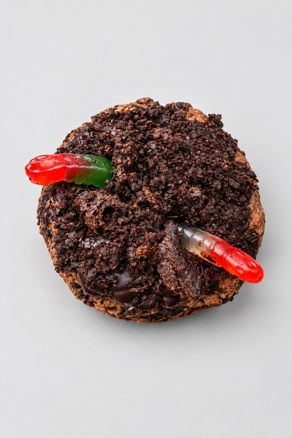 A small round chocolate cake topped with red gummy worms, presented on a wooden board outdoors with grass in the background.